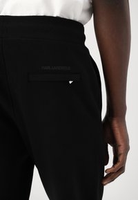 Zwarte broek met een gladde textuur, voorzien van een onopvallende achterzak en een zilveren accent. Het Karl Lagerfeld-logo is geperst.