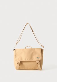 Beige lerret messengerbag med klafflås, justerbar stropp, topphåndtak, og grønn logo-detalj på forsiden. Kompakt rektangulær form.