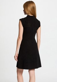 Black dress with a fitted bodice and flared skirt. Features a textured ribbed neckline and cap sleeves with scalloped edges.