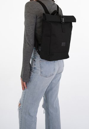 Sac à dos noir à rabat enroulant avec bretelles réglables, une fermeture à bouton-pression à l'avant et une poche latérale zippée ; fabriqué en tissu lisse et durable.