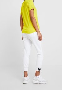 Gul t-shirt med korta ärmar kombinerat med vita joggerbyxor med svarta ränder vid fållen och vita sportskor.