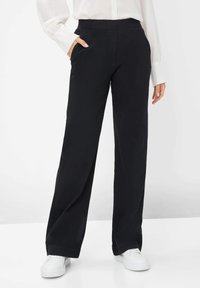 Schwarze, weit geschnittene Hose aus weichem Stoff, mit elastischem Bund und seitlichen Taschen, kombiniert mit weißen Sportschuhen.