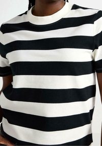 Camiseta de rayas blancas y negras hecha de suave algodón, con cuello redondo y mangas cortas, y con rayas horizontales uniformes.