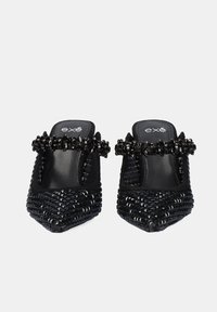 Mules trenzados negros con punta afilada, parte superior texturizada y una banda de cuentas a lo largo de la abertura. Forro interno suave y tacón plano.