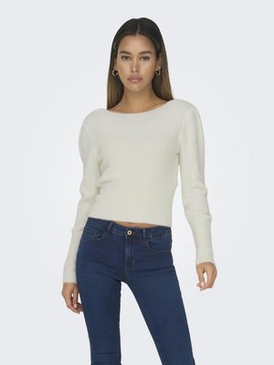Pull crème, court avec un col large et des manches longues, porté avec un jean taille haute bleu, présentant une finition texturée subtile.