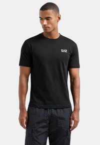 T-shirt nera a maniche corte realizzata in cotone. Presenta un logo EA7 bianco sul petto. Ha un girocollo e una vestibilità regolare.