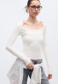 Μπλούζα μακρυμάνικη, στενή, από απαλό λευκό ύφασμα με τετράγωνη λαιμόκοψη. Συνδυάζεται με άνετο τζιν παντελόνι και ριγέ, ελαφρύ πουκάμισο δεμένο στη μέση.