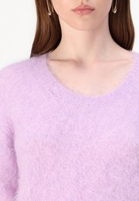 Šviesiai violetinė, pūkuota megztinis su plačiu iškirpimu ir minkšta tekstūra. Dizainas pasižymi subtiliu megztu raštu.