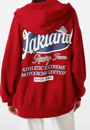 Punainen huppari, jossa takana iso "Oakland Racing Team Athletic Extreme Motocross Edition" -teksti ja ruutulippu-kuvio.