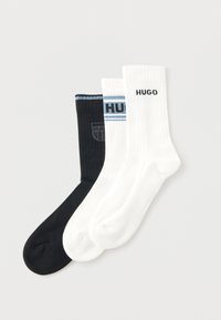 Τρία ζευγάρια κάλτσες: ένα μαύρο με λογότυπο, ένα λευκό με την εκτύπωση "HUGO" και ένα λευκό ριμπ με μπλε ρίγα στη ζώνη.