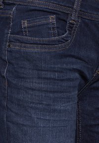 Mörkblå denimjeans med femfickorsdesign, synlig sömnad och en slät yta med svag blekning på framsidan.