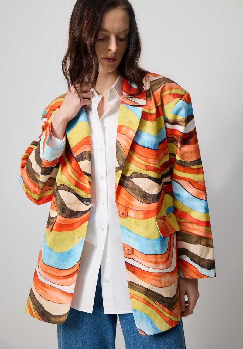 Collared blazer featuring an abstract wave pattern in orange, blue, and yellow hues. Made of smooth fabric with two front buttons and pockets.