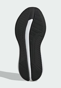 Semelle de chaussure de sport noire et blanche avec motifs texturés pour l’adhérence, présentée sur un fond clair uni.