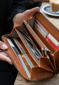 Brown leather wallet with multiple compartments, a striped fabric lining, and assorted cards visible inside. Zipper closure and classic design.