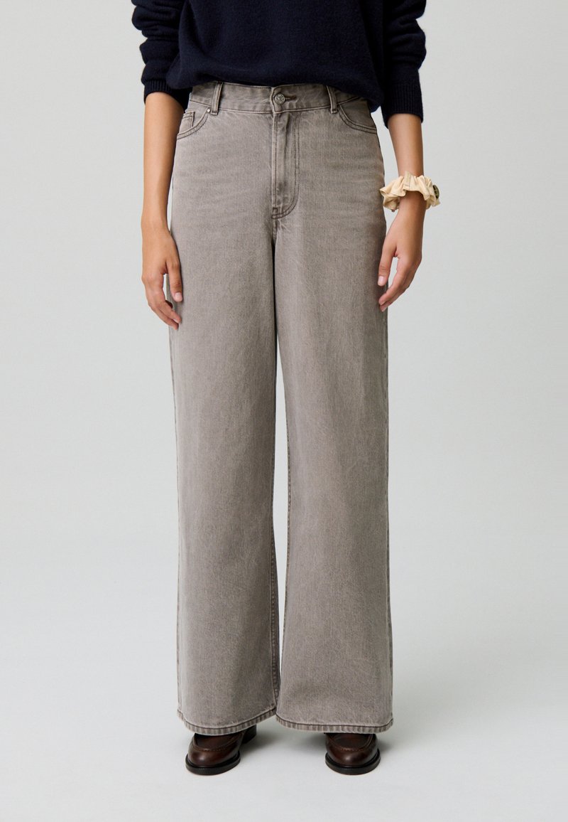 Pantalones de denim gris de pierna ancha con cintura alta, cierre frontal de botón y detalles de costura sutiles. La tela tiene una textura suave.