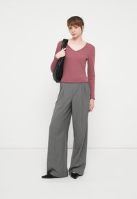 Μαρονού ribbed μπλούζα με μακριά μανίκια, v-λαιμό και οδοντωτό τελείωμα, συνδυασμένη με ψηλοκάβαλο γκρι παντελόνι με φαρδιά πόδια. Μαύρη τσάντα για έμφαση.