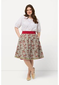 Valkoinen broderie anglaise -paita lyhyillä hihoilla, yhdistettynä kukkakuosisella beigehameella, jossa on punainen vyötärö ja vihreä korostushelma.