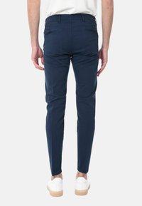 Chinos blu navy con una vestibilità slim, dotati di tasche posteriori e una leggera texture, abbinati a sneakers bianche e una camicia neutra.
