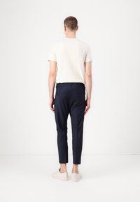 Granatowe spodnie o wąskim kroju i gładkiej teksturze, połączone z jasnobeżową koszulą z krótkim rękawem. Charakteryzują się minimalistycznym designem bez widocznych wzorów.