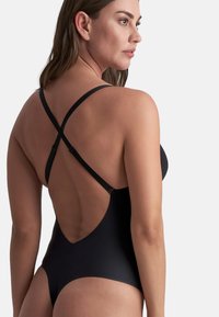 Zwarte éénstuk zwemkleding met een diepe ruguitsnijding, verstelbare kruisschuine bandjes en een soepele, strakke textuur. Minimalistisch ontwerp en hoge beenopeningen.