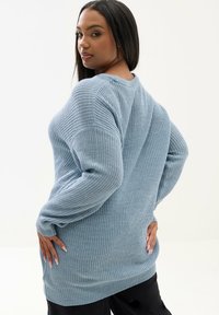 Suéter de manga larga en punto azul claro, con una tela texturizada, mangas anchas, aberturas laterales y un ajuste relajado.
