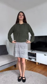 Donkergroene cropped hoodie gemaakt van gebreide stof, gecombineerd met een geruite, knielange rok in zwart-wit en zwarte platte schoenen.