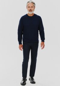 Granatowy sweter z okrągłym dekoltem, wykonany na drutach, z teksturowanym wzorem, w połączeniu z dopasowanymi ciemnymi spodniami i czarnymi butami na lace-up. Prosty i nowoczesny wygląd.