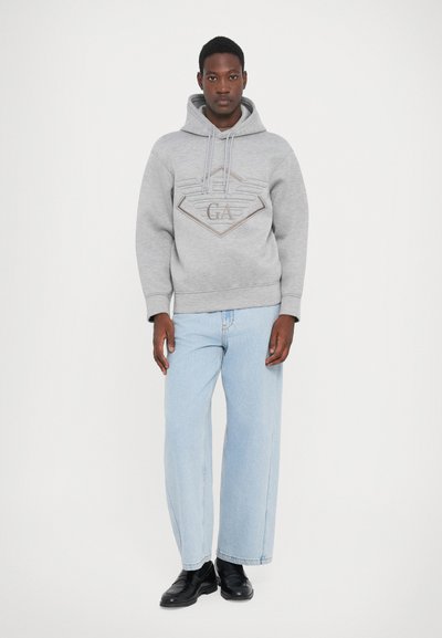 Grijze katoenen hoodie met een textuurlogo, capuchon met trekkoord en ribbelmanchetten, gecombineerd met lichtblauwe wijde jeans en zwarte schoenen.