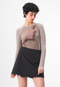 Schwarzer Wickelrock über einem beigefarbenen Langarmoberteil mit strukturiertem Muster; beinhaltet eine kleine rosa Tasche, die mit braunen Riemen befestigt ist.