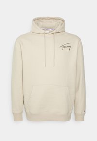 Sweat à capuche beige avec poche frontale, cordons et logo brodé "Tommy" sur la poitrine gauche.