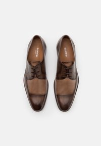 Chaussures habillées en cuir marron avec un design bicolore aux nuances contrastées, bout rond et laçage. Texture lisse avec un éclat subtil.
