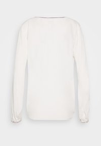 Blusa bianca a maniche lunghe con scollatura rotonda, polsini arricciati e un sottile dettaglio di cucitura sul collo, realizzata in un tessuto morbido.