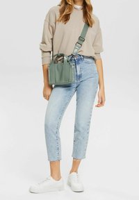 Sac à main en simili cuir vert avec double poignée et bandoulière réglable, porté avec un jeans cropped bleu clair et des baskets blanches à plateforme.