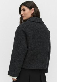 Mørkegrå uldblandingsjakke med krave, dybe skulderpartier og ribbede manchetter. Designet har en boxy silhuet.