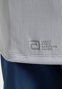 Svijetlosiva prozračna tkanina s logotipom "Abbott World Marathon Majors" u sivoj boji iznad tamnoplavih kratkih hlača ili hlača.