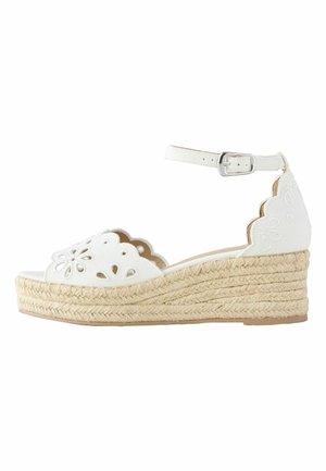 Biała sandałka espadryl na klinie z paskiem wokół kostki, falistymi krawędziami, kwiatowym wzorem wycięć i plecioną platformą z juty.
