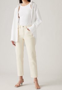 Canotta bianca sotto una camicia bianca oversized, abbinata a jeans a sigaretta color avorio e sandali con tacco beige a strappo.