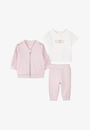 Roze zip-up jack met zijzakken, witte T-shirt met een gouden logo, en gecoördineerde roze joggers met gouden zijkanten.