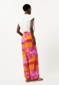 Wijduitlopende broek in een felroze, oranje en wit abstract patroon, gemaakt van een lichte stof met een elastische tailleband. Draag met een witte top.
