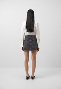 Denim mini skirt in black with frayed hem, paired with a white button-up shirt. Simple design, showing back view and flat shoes.