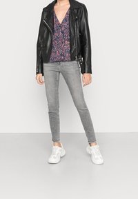 Giacca biker in pelle nera sopra una maglietta floreale a scollo a V nei toni del blu navy, rosa e bianco. Jeans skinny grigi con orli sfilacciati. Sneakers bianche.