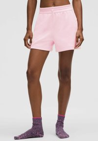 Rozā kokvilnas šortus ar elastīgu jostu un sānu kabatām apvieno ar teksturētām violētām zeķēm, kurām ir rozā aproce.