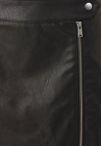 Jupe en cuir noir avec une surface texturée, dotée d'une fermeture éclair latérale argentée et d’un détail à pression à la ceinture. Design classique et finition soignée.