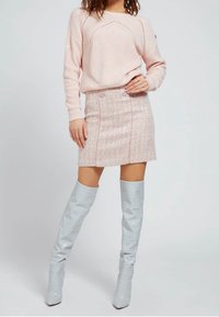 Vaaleanpunainen neulottu villapaita, jossa on teksturoitu kuvio, yhdistettynä vaaleanpunaisiin laikullisiin hameeseen, jossa on kaksi etupainiketta ja hopeiset polvigamaanikengät.