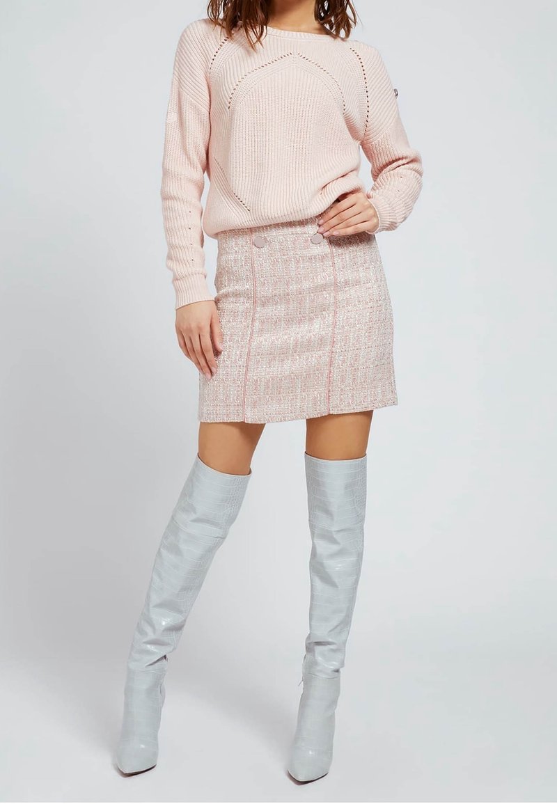 Vaaleanpunainen neulottu villapaita, jossa on teksturoitu kuvio, yhdistettynä vaaleanpunaisiin laikullisiin hameeseen, jossa on kaksi etupainiketta ja hopeiset polvigamaanikengät.