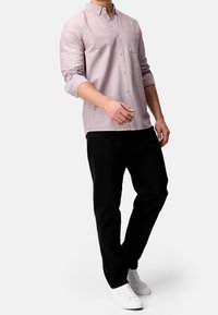 Helles rosa Hemd mit Knopfleiste aus strukturiertem Stoff, mit einer Brusttasche und hochgerollten Ärmeln, kombiniert mit schwarzen Hosen und weißen Sneakers.