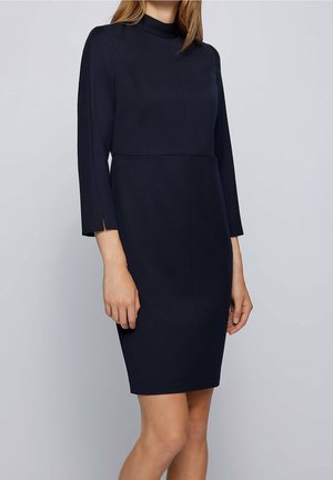 Mörkblå, knälång klänning med hög krage, långa ärmar och sidopluppar. Tillverkad av ett slätt, strukturerat tyg med en figursydd siluett.