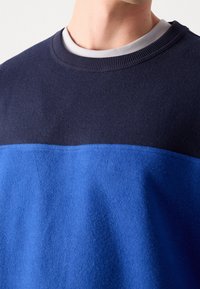 Sudadera azul y azul marino con cuello redondo, tejido texturizado y diseño bicolor con acabado liso y puños acanalados.