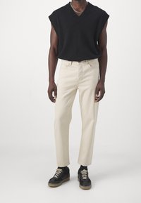 Suéter sin mangas negro con escote en V, jeans rectos de un beige claro y zapatillas negras con suelas de color arena. Diseño sencillo, estilo casual.