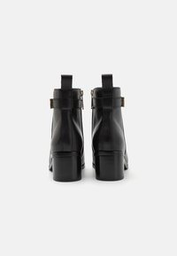 Schwarze Leder-Ankle Boots mit rechteckiger Spitze, Blockabsatz, Reißverschluss hinten und dekorativem Schnallen-Detail an der Seite. Glatte Textur und minimalistisches Design.